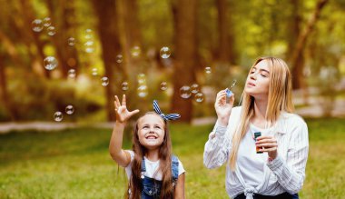 Neşeli anne ve kızı parkta piknik yaparken eğleniyor ve sabun köpüğü yakalıyor. Aile Hafta Sonu
