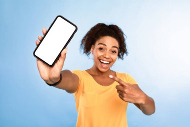 Şuna bak, cep telefonu ekran modeli. Heyecanlı Afro-Amerikan kadın akıllı telefonu işaret ediyor mavi arka planda boş ekran, seçici odaklanma. Mobil uygulama, web sitesi veya çevrimiçi reklam için boşluk