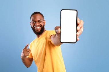 Heyecanlı Afrikalı Amerikalı rahat giyinen adam cep telefonuna işaret ediyor mavi ekranlı arka plan, web sitesi ya da mobil uygulama tasarımı için boşluk. Cep telefonu ekran modeli. Seçici odak