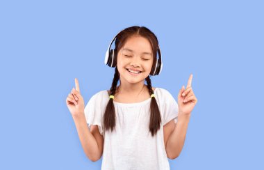 Küçük Müzik Aşığı. Kulaklıklı Asyalı Kız Mor Stüdyo Arkaplanında Duran Şarkı Dinlerken eğleniyor.