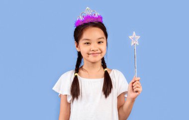 Küçük Prenses Konsepti. Tapılası Japon kızı elinde sihirli değnekle Mor Stüdyo Arkaplanına gülümsüyor..