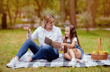 Şehir parkında aile pikniği yaparken kitap okuyup tartışan pozitif anne ve küçük kız. Hafta sonu Konsepti