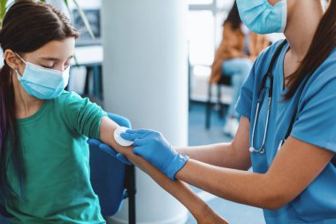 Yüz maskesi takan hemşire ve eldivenlerin çocuk derisini dezenfekte etmesi, sağlık merkezine enjeksiyondan önce omzuna pamuk pedi sürmesi, klinik geçmişi. Grip koronavirüsü tedavisi kavramı