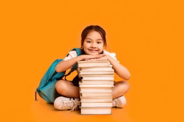 Son olarak, okula dönüş. Kitap rafında oturan tatlı Asyalı kız öğrenci sarı stüdyoda okula gitmeye hazır..