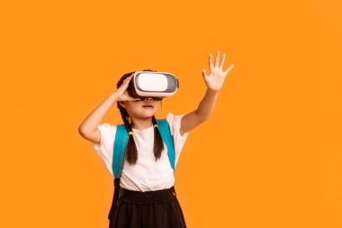 Okul Yenilikleri. Sanal gerçeklik gözlüğü takan Asyalı Liseli Kız Sarı Arkaplan 'ın üzerinde duran sanal gerçeklik deneyimi yaşıyor. Stüdyo Çekimi