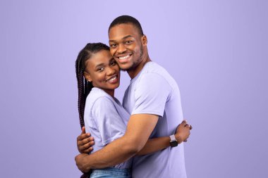 Mor arka planda poz veren neşeli Afrikalı Amerikalı çiftin portresi, mutlu siyah erkek ve kadın kucaklaşması ve kameraya gülümsemesi,