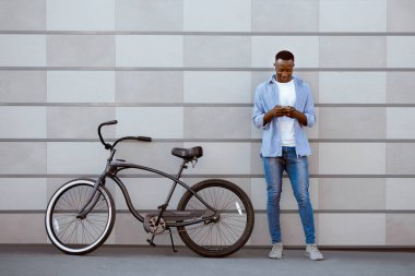 Kulaklıklı mutlu siyah motosikletçi. İnternette yeni müzik arıyor. Tuğla duvarın yanındaki akıllı telefondan.