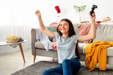 Playstation 'da video oyunu kazanan mutlu Hintli genç kız içeride zaferi kutluyor. Oyun kolu olan neşeli ergen oyuncu bilgisayar oyunu oynuyor, ev eğlencesinin tadını çıkarıyor.
