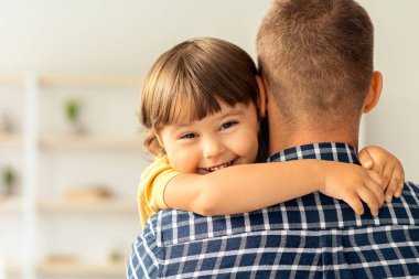 Babamı çok seviyorum. Babasını kucaklayan, kameraya gülümseyen, tanınmayan bir adamın arka plandaki mutlu küçük çocuğun portresi.