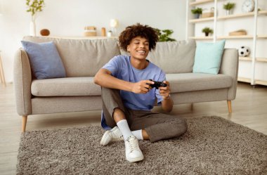 Çevrimiçi video oyunları oynayan, evinde yerde oturan bir sürü pozitif siyahi genç oyuncu. Afro-Amerikalı ergenler kapalı yerlerde eğleniyorlar.