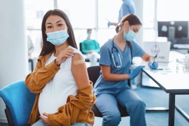 Grip aşısı konsepti. Corona virüsü aşısı olduktan sonra kolunda yapıştırıcı bandaj olan, cerrahi maskeli bir kadının portresi. Antiviral Enjeksiyon