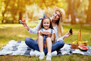 Yaz neşesi. Anne ve kızı piknik yapıyor, karpuz yiyor, parkta karpuz oturuyor, kameraya gülümsüyor.