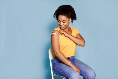 Gülümseyen Afrikalı Amerikalı kadın gribe karşı aşı oluyor, mavi arka planda yara bandı ile kol gösteriyor, boş alan. Kadın hasta grip aşısı oluyor. Nüfus bağışıklığı