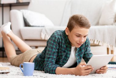Evde çalışırken dijital tablet kullanan, odasında yerde yatan bir öğretmen.