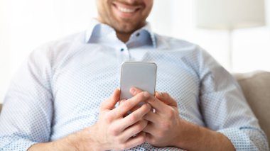 İnternete göz atıyorum. Neşeli yakışıklı adam akıllı telefonunu kullanıyor. Evdeki kanepede oturuyor.