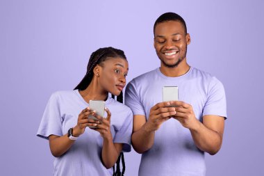 Meraklı siyah kadının portresi, erkek arkadaşının akıllı telefonuna bakmaya çalışan, elinde aletini tutan ve sohbet eden gülümseyen bir adam Violet stüdyosunun arka planında tek başına duran bir çift. Güvensizlik Konsepti