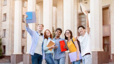 Neşeli çeşitli öğrenciler üniversite binasının önünde kameraya gülümseyen pozlar veriyor. Yüksek Öğrenim Konsepti