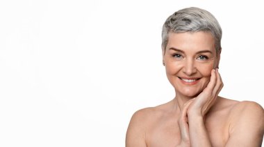 Olgun Güzellik. Çekici, çıplak, orta yaşlı bir kadının portresi tenine dokunuyor ve kameraya gülümsüyor.