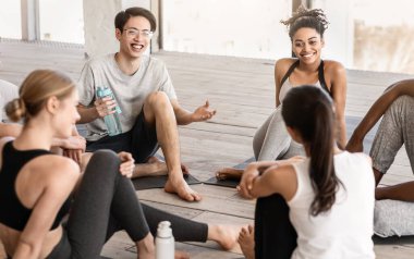 Yoga dersinden önce stüdyoda iletişim kuran, yerde oturup sohbet eden bir grup genç.