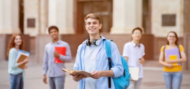 Üniversite öğrencisi. Neşeli Millennial Guy, çok ırklı öğrenciler arasında duruyor Açık Üniversite Binası 'nın yakınında, Kameraya gülümsüyor