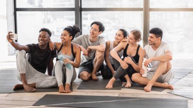 Stüdyoda çalıştıktan sonra akıllı telefondan selfie çeken yoga sınıfının mutlu üyeleri.