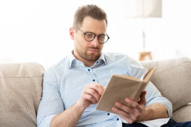 Eğitici kavram. Özelliklerinde odaklanmış iş adamı kitap okuyor modern apartmandaki koltukta dinleniyor, seçici odaklanıyor.