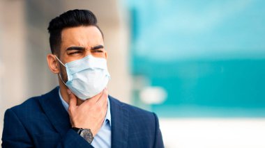 Hasta Arap yönetici COVID-19 salgını, yüz maskesi takan genç ortadoğulu işadamı, ofis binasının yanında dururken, boğaza dokunurken, soğuk algınlığı, baca ya da koronavirüsten muzdaripken çalışıyor.