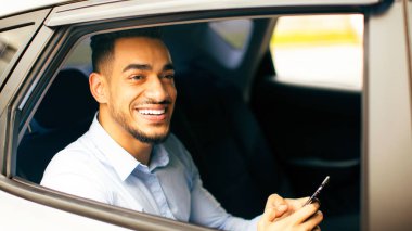 Positif Ortadoğulu işadamı e-postaları kontrol ederken arabasıyla ofise gidiyor, arka koltukta oturuyor ve akıllı telefon kullanıyor, yakın plan fotoğraf çekiyor, dışarıdan çekiliyor, yan görünüm, boşluk kopyalıyor.