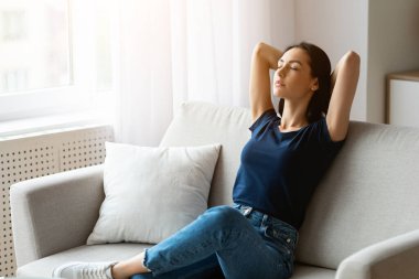 Haftasonu Gevşemesi. Huzurlu bir kadın ellerini başının arkasında tutarak evinde gözleri kapalı bir şekilde oturuyor. Boş Boşluk