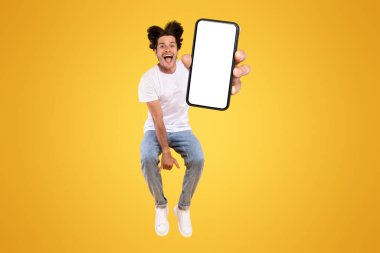 Yakışıklı sakallı genç adam yeni mobil uygulama öneriyor, dikey kolaj. Akıllı telefonu tutan heyecanlı adam, beyaz beyaz ekranı gösteriyor, turuncu sarı stüdyo arka planında zıplıyor.