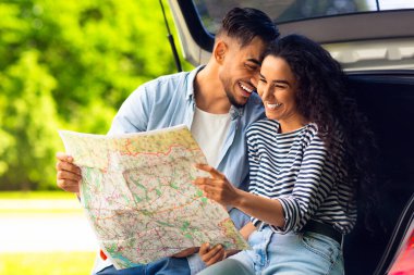 Mutlu genç aşıklar araba bagajında oturup yol haritasını izlerken kucaklaşıyorlar, kopyalama alanı. Yakışıklı Arap adam güzel kız arkadaşıyla bağ kuruyor, araba gezisinde mola veriyor.