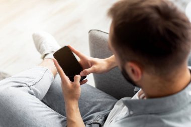 Evinde boş ekranı olan akıllı telefonu kullanan genç bir adam. Mobil uygulama tasarımı için model. Milenyum adamı elinde modern bir alet tutuyor, web sitesi ya da reklam için boş bir alan
