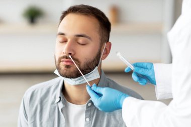 Doktor evde erkek hasta var mı diye covid-19 PCR testi yapıyor. Milenyum adamı içeride koronavirüs tanılama prosedürü uyguluyor. Viral hastalık önleme ve tedavi kavramı