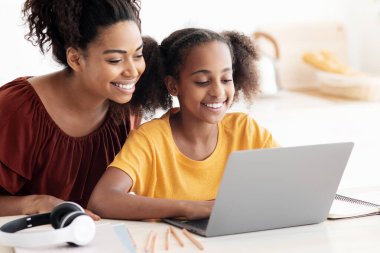 Tatlı siyah anne ve çocuk birlikte dizüstü bilgisayar kullanıyor, mutfak masasında oturuyor, sarılıyor ve bilgisayar ekranına bakıyor, birlikte vakit geçiriyor, çizgi film izliyor, fotokopi çekiyor, yakın çekim fotoğrafı çekiyor.