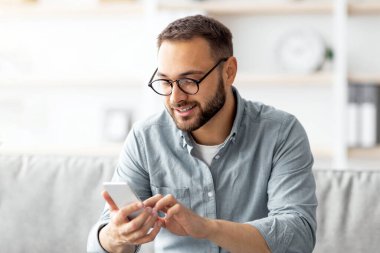 Gözlüklü olumlu genç adam koltukta oturuyor cep telefonuyla ve içerideki arkadaşına mesaj atıyor. Milenyum Kafkasyalı bir adam mesaj yazıyor, video görüşmesi yapıyor ya da evde internet yayını yapıyor.