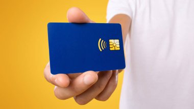 Elinde plastik kredi kartı tutan tanınmayan bir adama yakın çekim. Perakende, alım, ödeme, dijital para, bankacılık konsepti. Pankart, panorama, sarı turuncu stüdyo arka plan