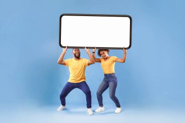 Milenyum Afro-Amerikan çifti ellerinde mavi stüdyo arka planında boş ekran olan büyük bir akıllı telefon tutuyorlar. Reklam, mobil uygulama ya da yeni web sitesi için bir model. Cep telefonu görüntüleme şablonu