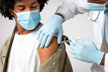 Aşı kavramı. Doktor, siyah erkek hastaya iğne ya da aşı yapıyor, koluna şırınga sokuyor, maskeli Afrikalı Amerikalı genç adam Covid-19 'a karşı aşı oluyor.