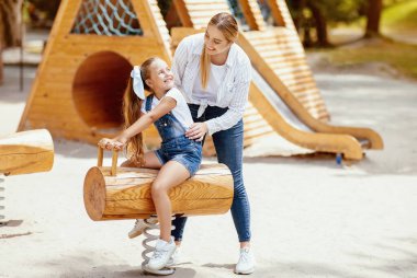 Anne, kızı salıncakta sallarken dışarıda eğleniyor. Hafta sonu tatili konsepti. Boşluğu Kopyala