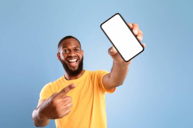 Yeni harika mobil uygulama. Aşırı neşeli Afro-Amerikalı adam mavi arka planda beyaz ekranlı akıllı telefonu işaret ediyor. Cep telefonu görüntüleme şablonu, reklam veya web sitesi için alan