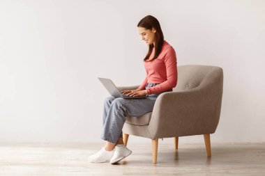 Mutlu genç bayan koltukta oturuyor, dizüstü bilgisayar kullanıyor, uzaktan çalışıyor ya da iş görüşmesi yapıyor, boş yer var. Milenyum Kafkasyalı kadın online ders alıyor ya da webinar seyrediyor