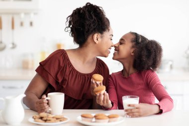 Afro-Amerikan anne ve kızını sevmek, evde birlikte vakit geçirmek, abur cubur yemek, süt içmek, ev yapımı hamur işleri yemek, birbirlerine burunlarla dokunmak ve gülümsemek, kopyalama alanı yaratmak.