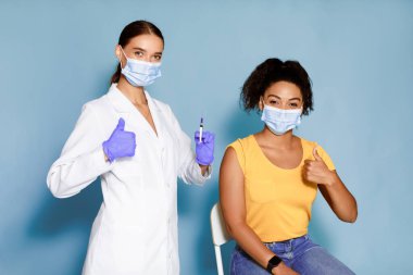 Grip aşısını onaylayan maskeli genç Afrikalı Amerikalı kadın grip aşısından önce işaret veriyor, antiviral bağışıklık öneriyor.