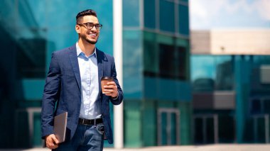 Bilgisayarlı ve kahveli neşeli orta doğulu genç işadamı caddeden modern ofis binasına doğru yürüyor, sabah işe gidiyor, fotokopi alanı olan bir panorama.