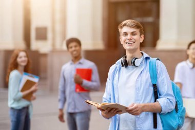 Üniversite öğrencisi. Neşeli Millennial Guy, çok ırklı öğrenciler arasında duruyor Açık Üniversite Binası 'nın yakınında, Kameraya gülümsüyor