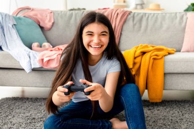 Evde eğleniyorum. Çevrimiçi video oyunları oynayan mutlu Hintli genç kız, yerde kontrolörle oturuyor, içeride. joystick 'i olan komik ergen bilgisayar oyunlarıyla meşgul.