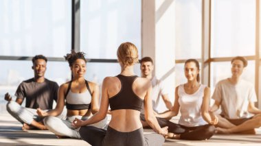 Profesyonel Yoga koçu, bir grup gençten ders alıyor, Lotus pozisyonunda yan yana oturuyorlar, Antrenörün arkadan görünüşü...