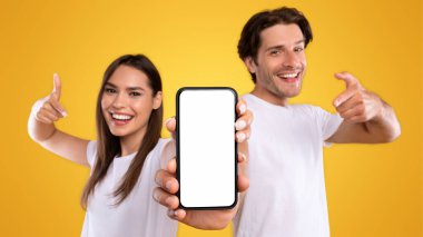 Bu yeni uygulamayı kullan. Neşeli milenyum çifti portresi beyaz ekranlı akıllı telefonu işaret ediyor, mobil uygulama öneriyor, web sitenizi tanıtıyor, tasarım için makara yapıyor. Seçici odak