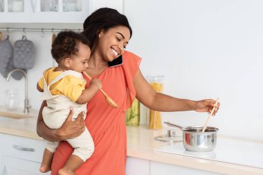Aynı anda hem de. Gülümseyen kadın bebeğini kucağında tutuyor, mutfakta cep telefonuyla konuşuyor, mutlu Afrika kökenli Amerikalı anne tencerede yemek pişiriyor ve küçük çocuğuyla ilgileniyor.