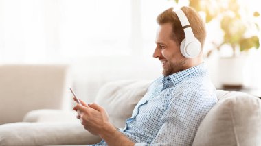 Boş zaman. Kablosuz kulaklıkla müzik dinleyen gülen adamın yan görüntüsü, telefonla koltukta oturması, kopyalanması...